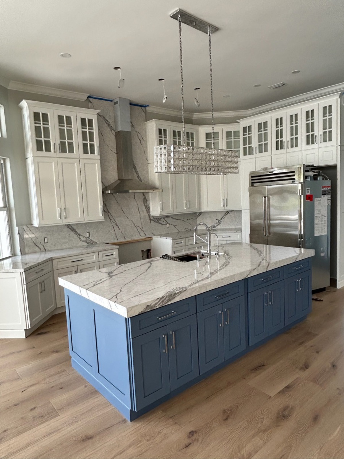 Luxury kitchen renovation with white upper cabinets, blue island, marble countertops, marble backsplash, and hardwood flooring